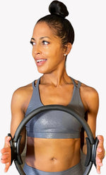 A model holding a round piece of exercise equipment wearing the Glitz & Glam sports bra. 